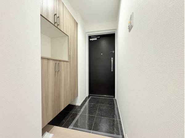 モダンな黒い玄関ドアと、対照的な明るい木目調のシューズインクローゼット