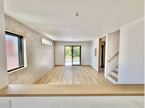 キッチンからリビングダイニングが見え、窓の外には駐車場と木々が見えます