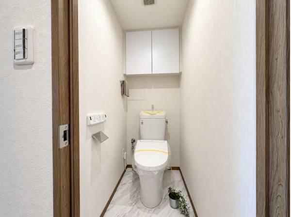 上部の収納で日用品を整理できる、白を基調とした清潔感のあるトイレです。
